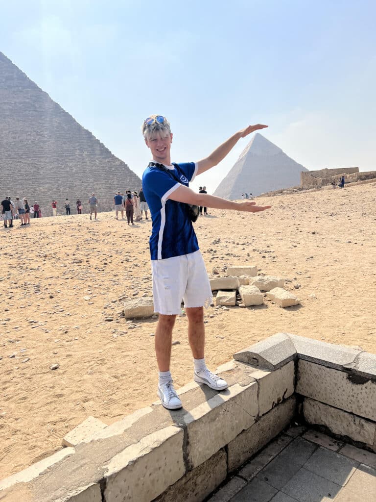 A picture of Tom holding his arms out to make it look as if he is holding one of the pyramids of Giza.