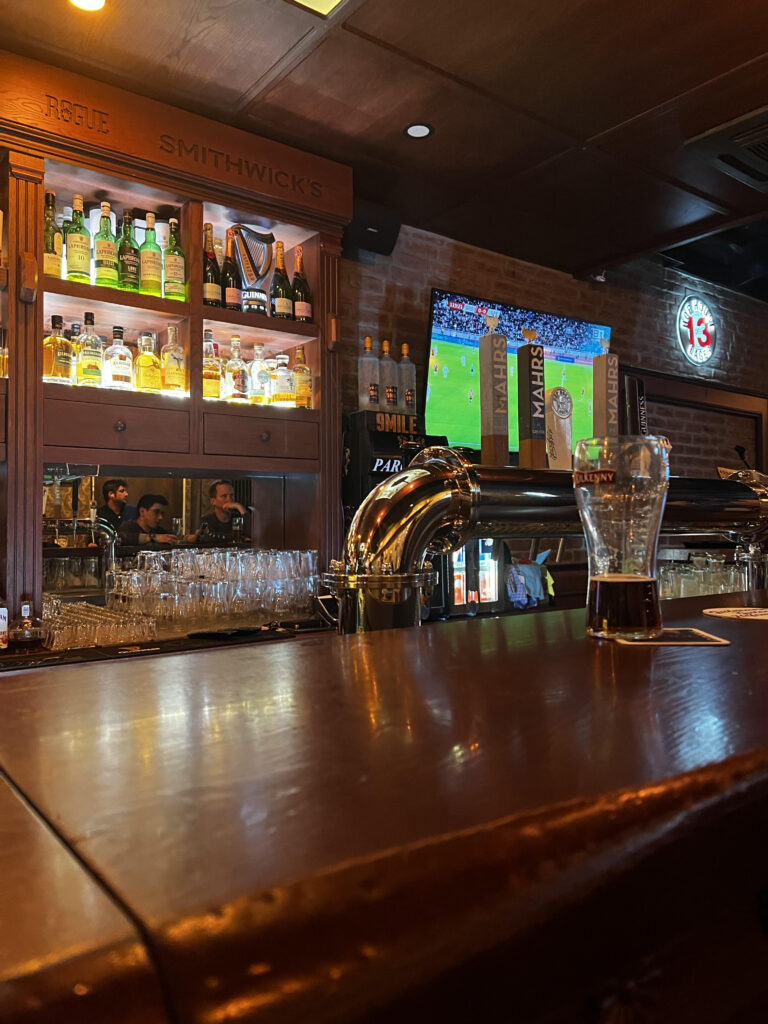 An Image taken from a bar stool overlooking the bar and a football match from a TV in the background.