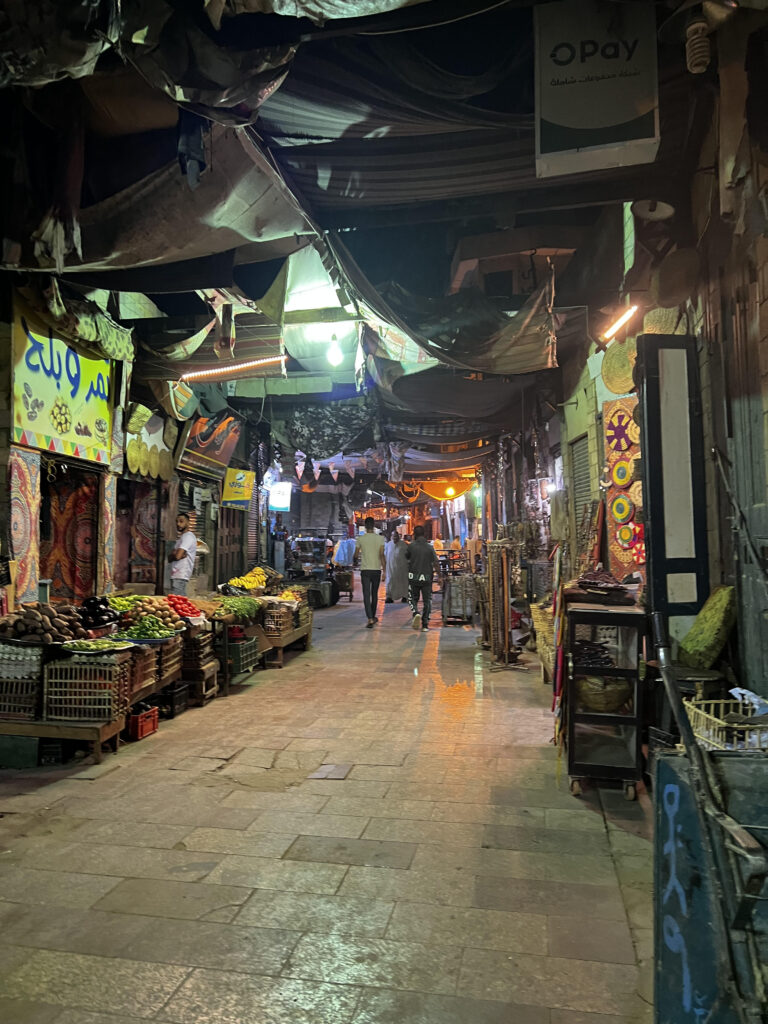 A local market in Aswan at night with much fruit and ornaments on display.