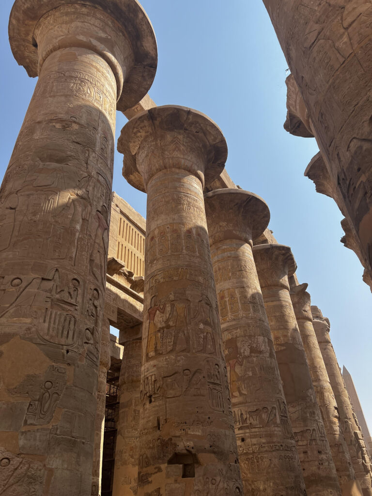 6 pillars and an obelisk in the background somewhere in Karnak Temple