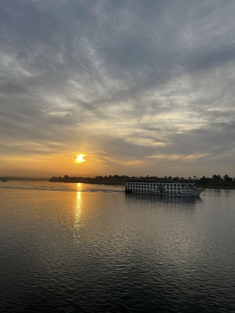 From the persepective of the Authors Nile boat, a picture of another Nile Cruise moving in foreground of the West side of the Nile in the background