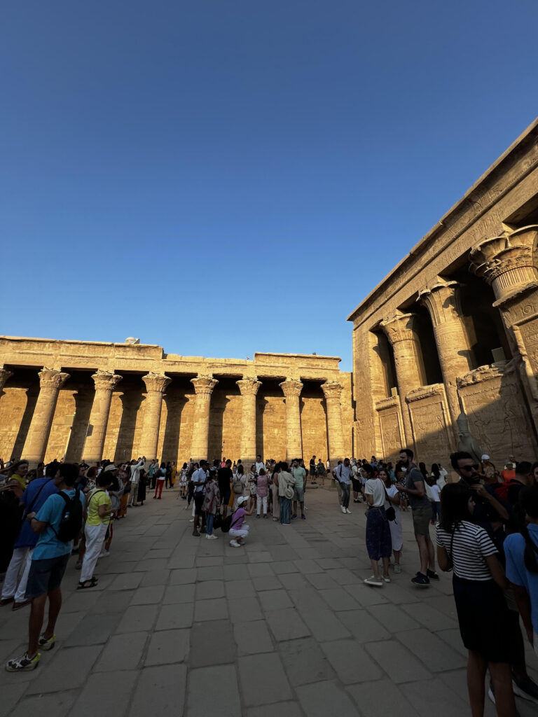 The courtyard of the Temple of Horus at dawn with many tourists.