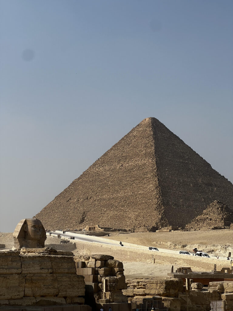 A shot of the Sphinx's head in the foreground of the Great Pyramid of Giza in the background.