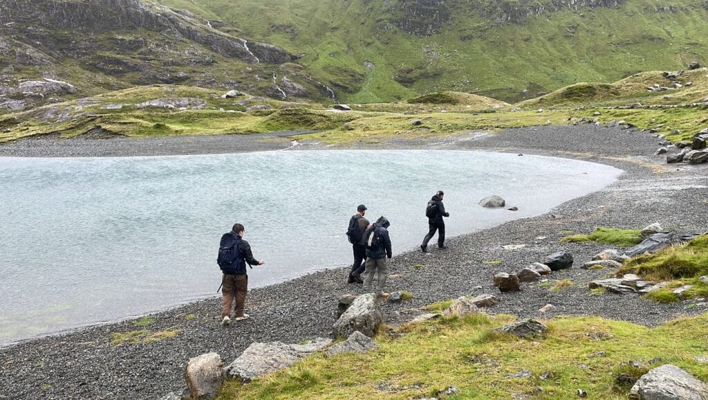 A few friends walking on the rocky beach next to a lake on the way up Snowdon.