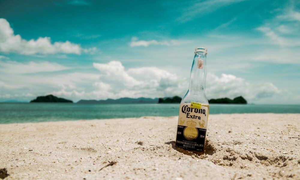 A Corona bottle wedged in the sand along a tropical beach.