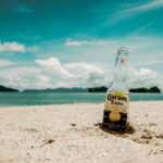 A Corona bottle wedged in the sand along a tropical beach.