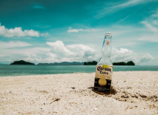 A Corona bottle wedged in the sand along a tropical beach.