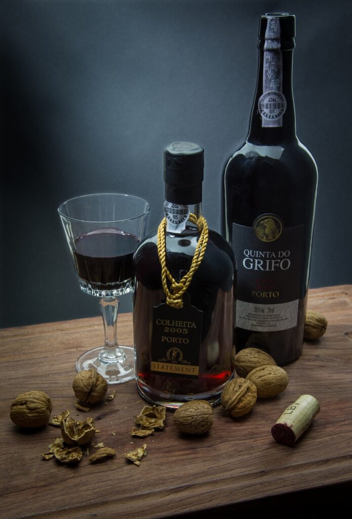 Two separate bottles of port wine next to a glass of port surrounded by nuts.