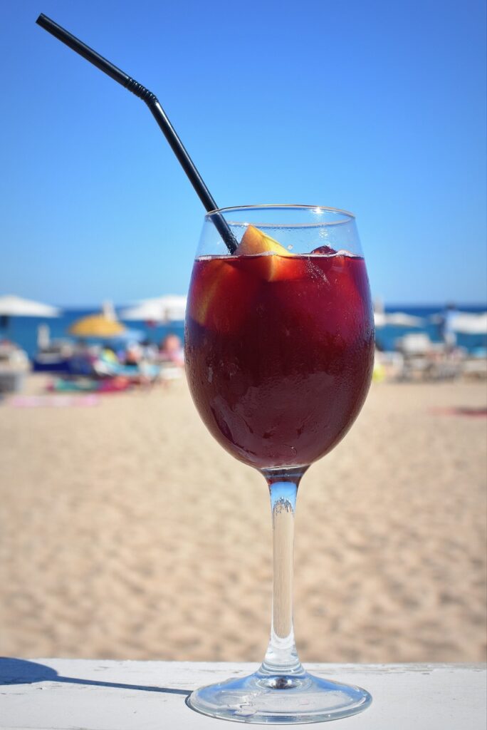 A glass of sangria in the foreground of a beach in the background.