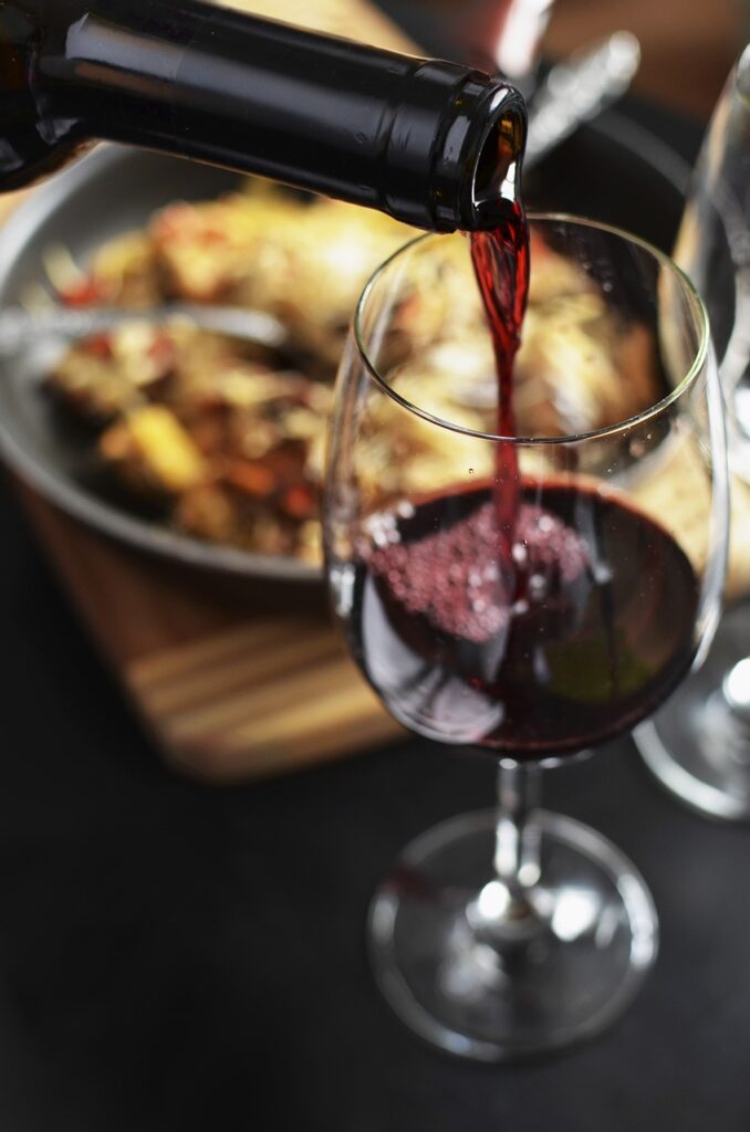 A glass of wine being poured in the foreground of a meal.