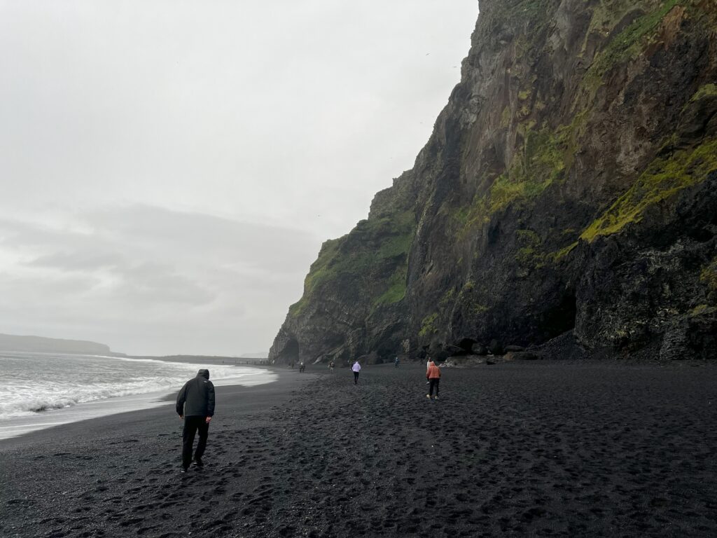 The Víkurfjara Black Sand Beach on a cloudy day with the view of the water and the massive cliffs.