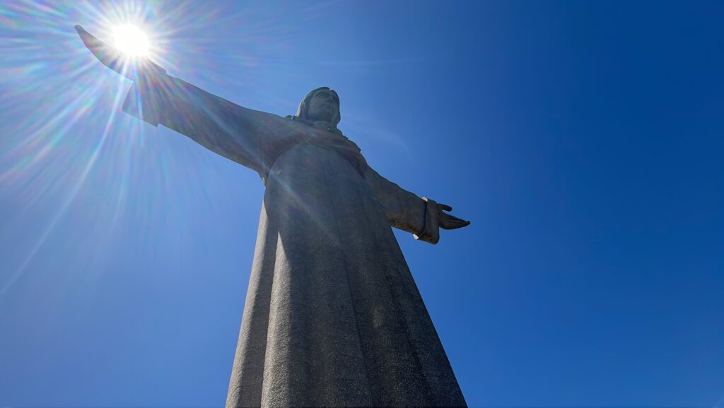 A close up of the Santuário de Cristo Rei from the viewpoint of the top of the tower. Coincidentally, the right arm of the statue has the sun on top of it as if it is holding the sun.