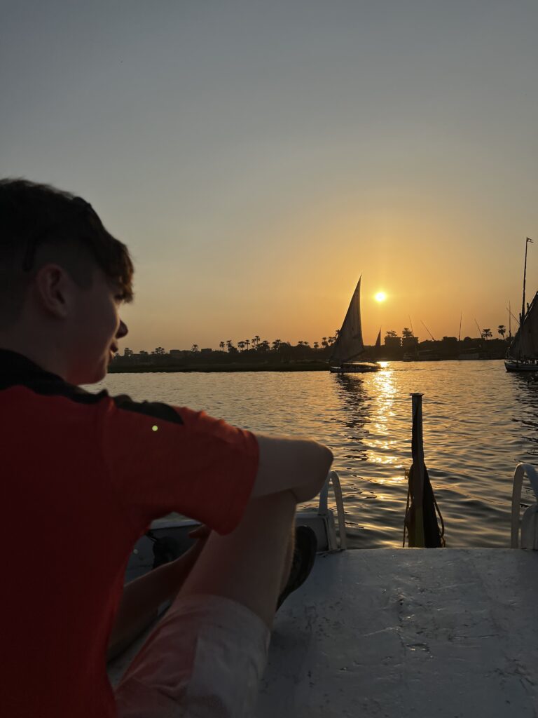 A image of a man sitting looking out at the sunset from the perspective of a small fishing boat in Egypt.