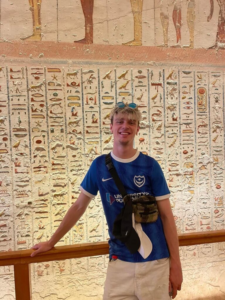 The author, Tom, wearing a cross body bag in front of some Hieroglyphics inside of an Egyptian tomb.