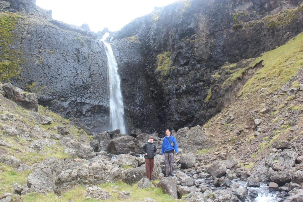 The author stood next to his brother next to a random waterfall in Iceland.