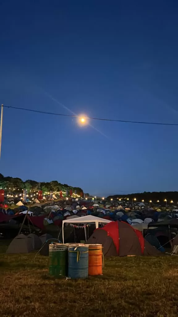 Tents in a field lit up by a sky about an hour prior to sunrise.